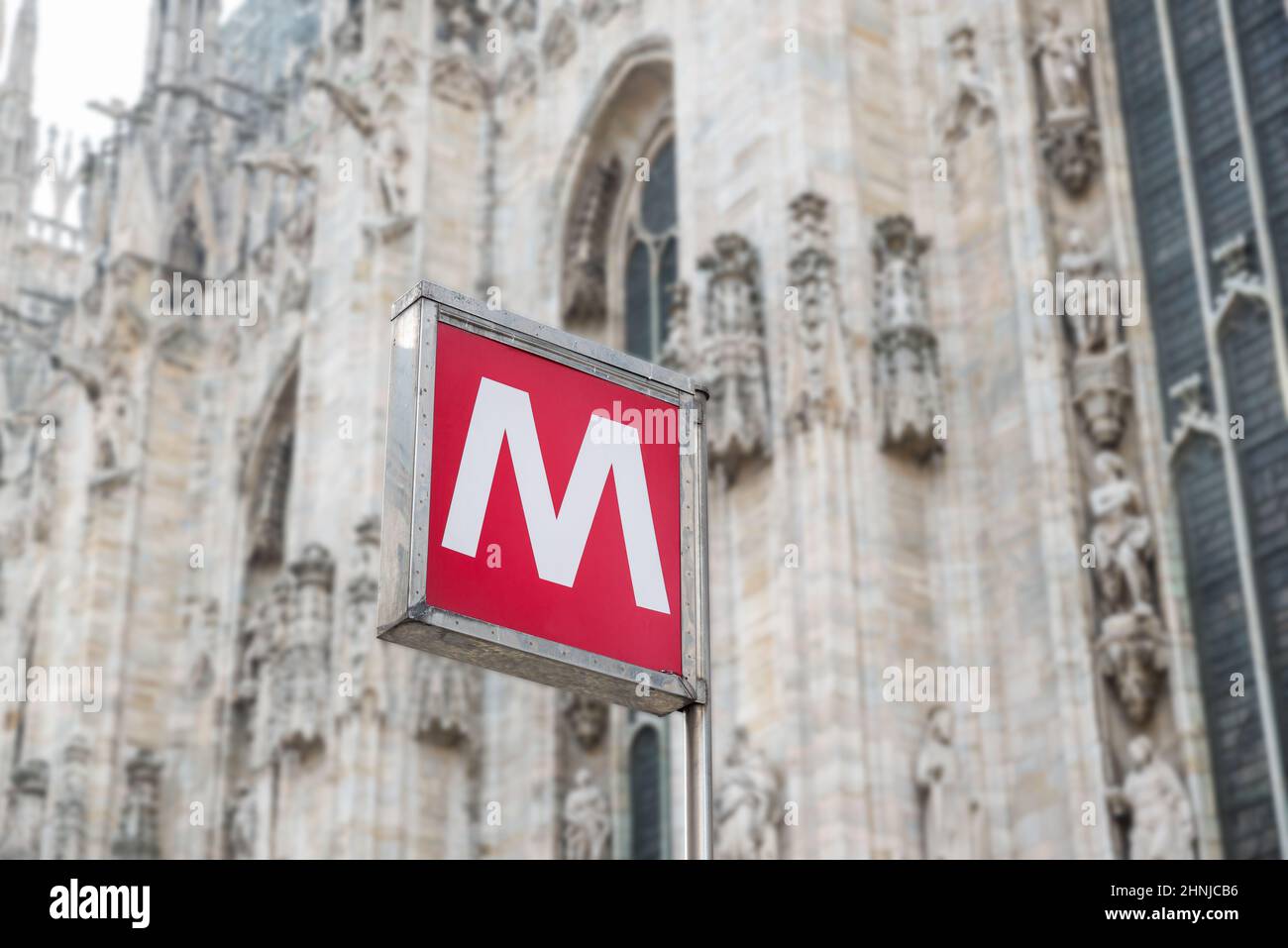 Señal roja del metro en la estación de metro, letra M. Concepto de transporte urbano. Piazza del Duomo, con la borrosa Catedral de Milán en el fondo, Italia Foto de stock