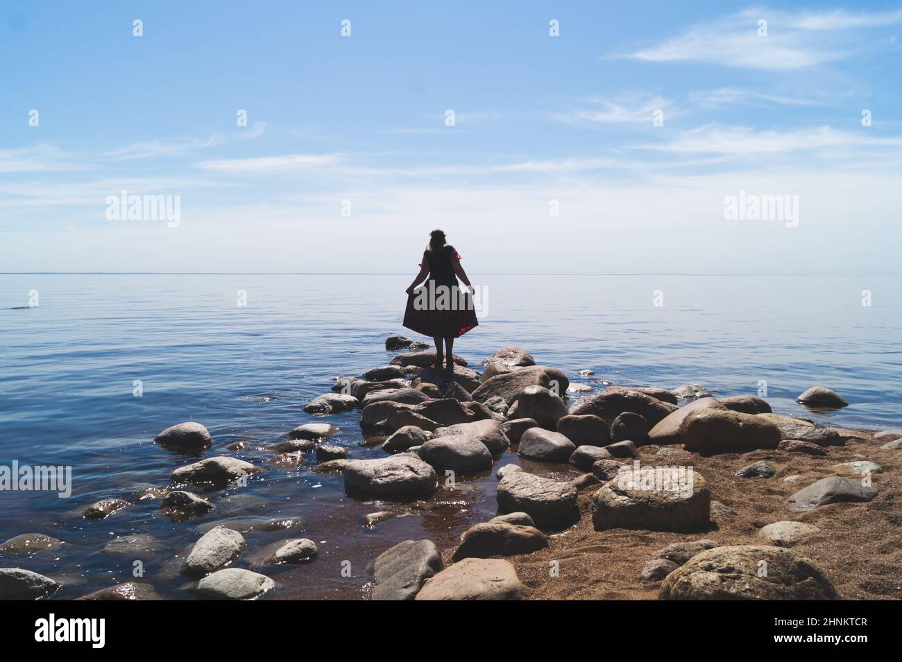 Silueta de una mujer de pie sobre piedras en la playa. Hermoso paisaje veraniego con línea horizonte Foto de stock