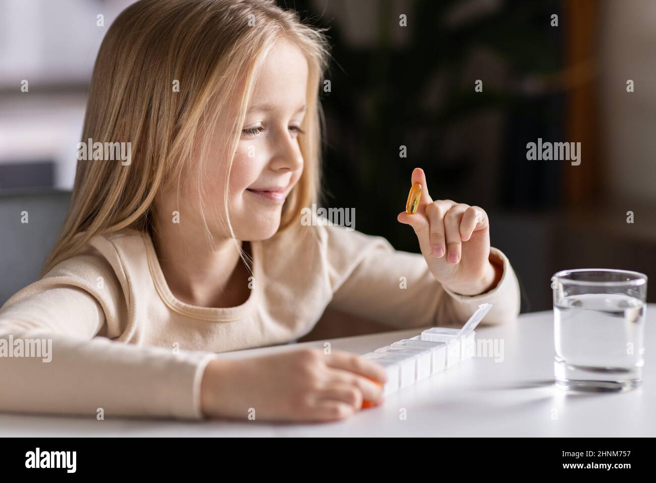 Niña Caucásica en pijamas tomando vitamina omega-3 natural de la caja de  plástico en la cocina en casa temprano por la mañana. Un niño adorable toma  suplementos. H Fotografía de stock -