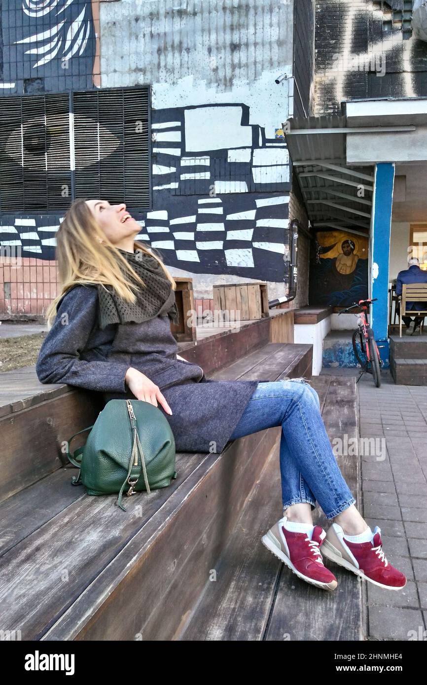 Una joven se sienta en una escalera de madera y se ríe, levantando la cabeza Foto de stock