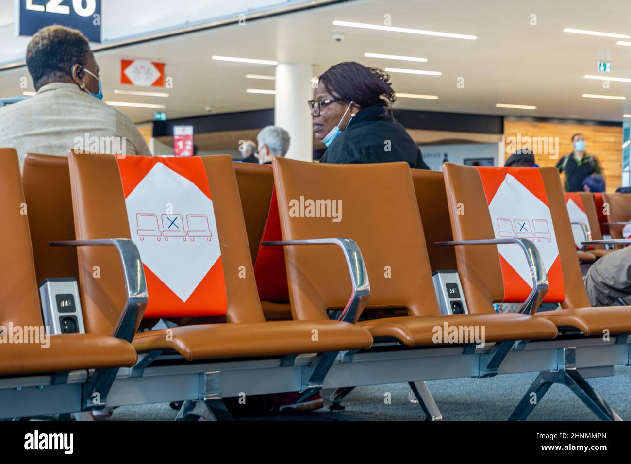 Charles de Gaulle, París, 13 de enero de 2022 - Hombre y mujer negros en conversación detrás de asientos vacíos con señales de distanciamiento social en el aeropuerto Foto de stock