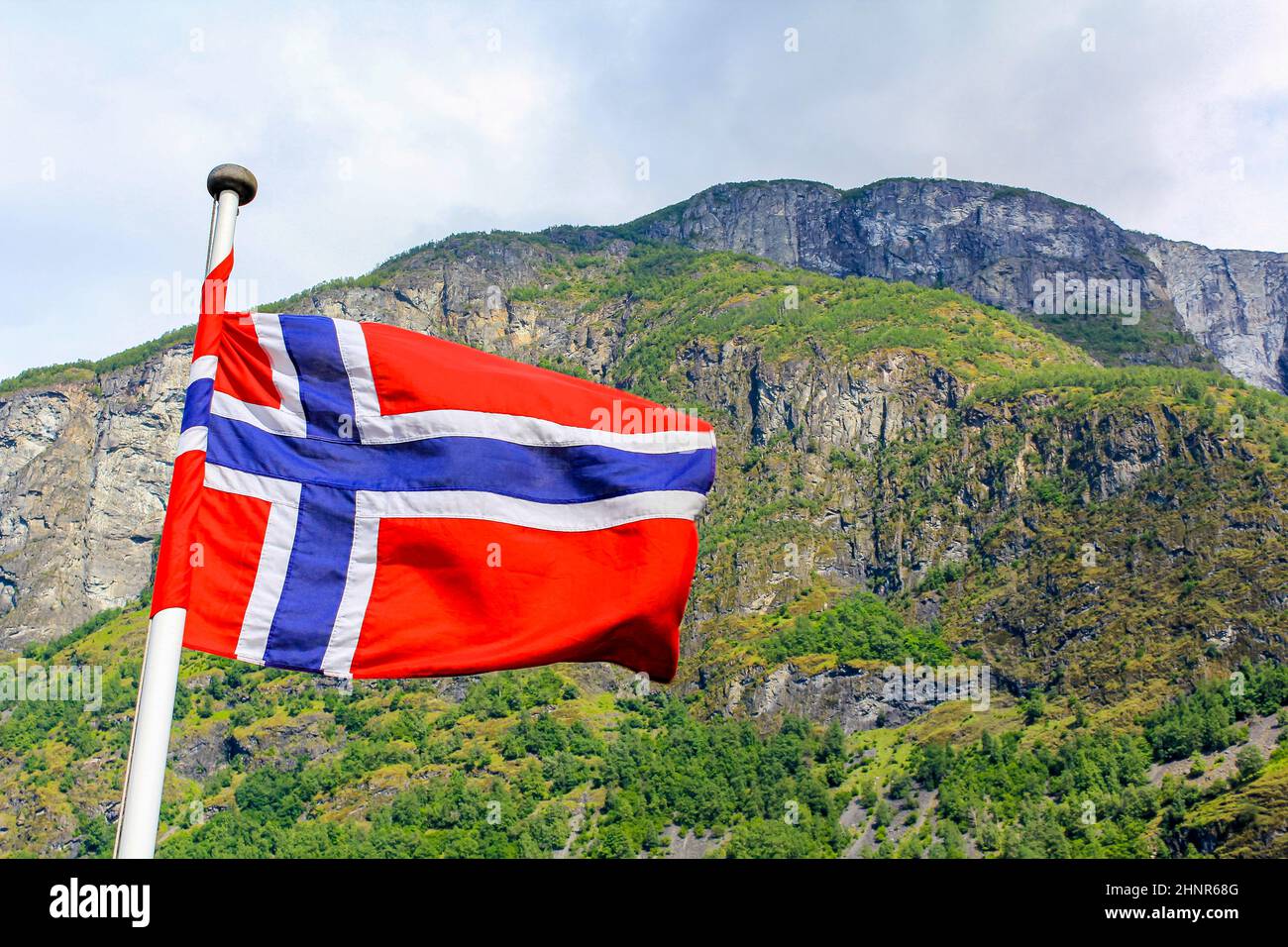 La bandera nacional de Noruega en el viento áspero y cielo azul con nubes. Foto de stock