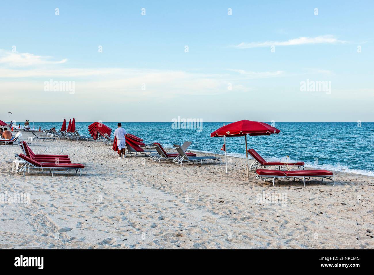 El chico del hotel recoge las camas rojas de la furgoneta en la playa del sur al final del día soleado en Miami Foto de stock