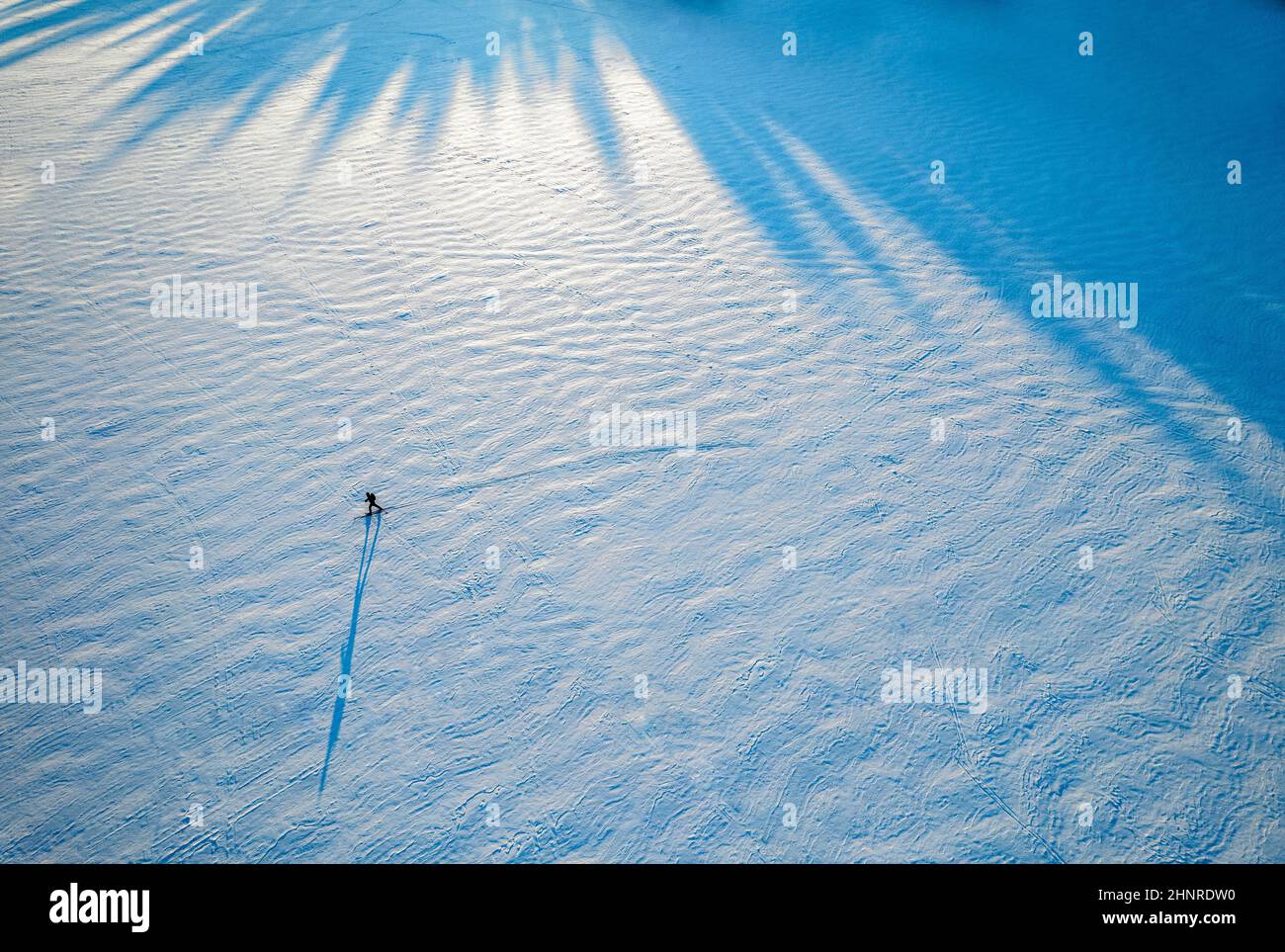 Figura diminuta y sombra de esquiador solitario en lago congelado, Maine Foto de stock