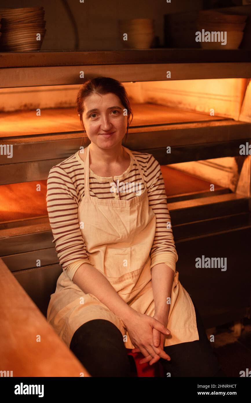mujer en delantal cerca del horno caliente en la panadería Foto de stock