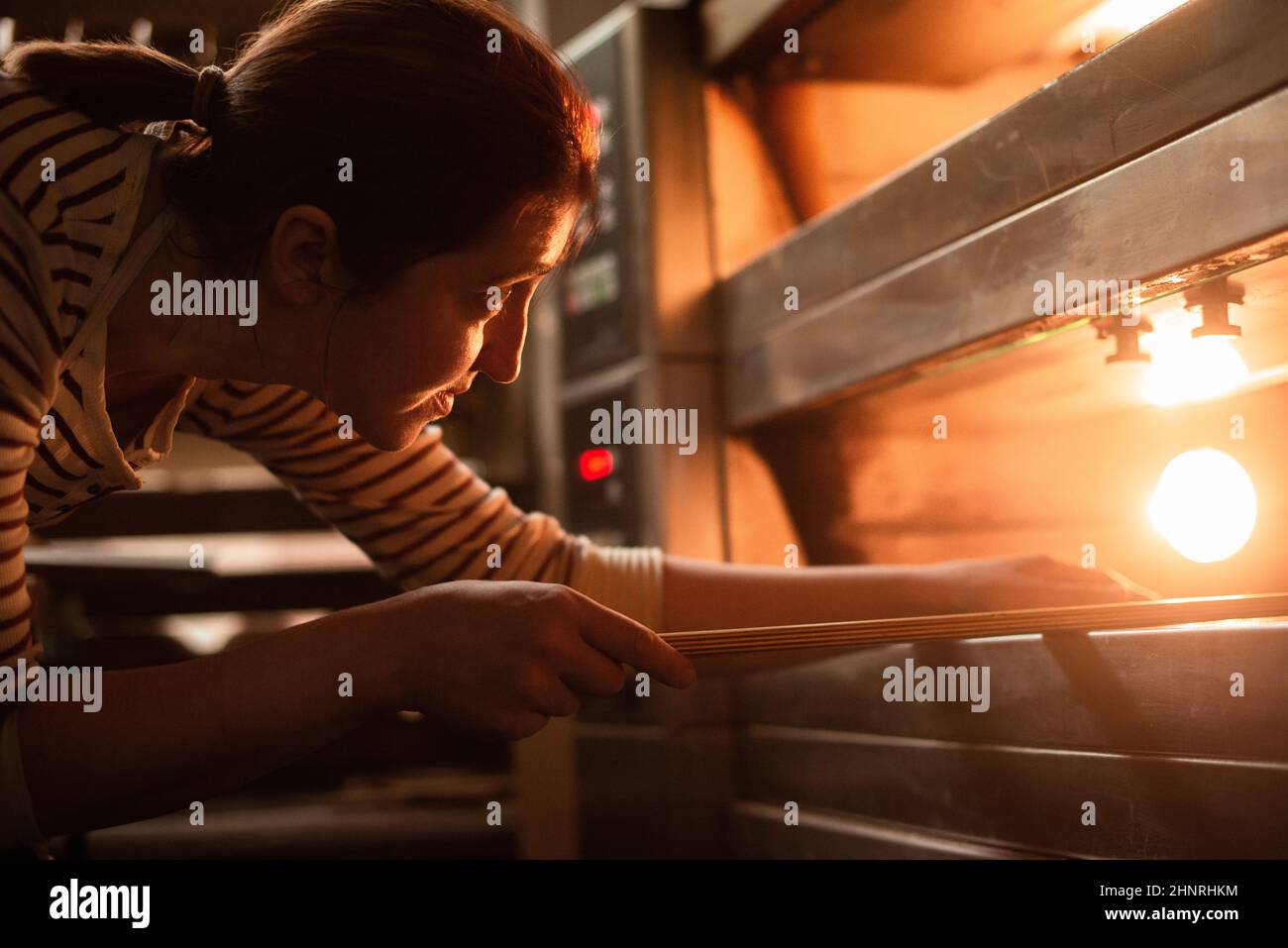 mujer en delantal cerca del horno caliente en la panadería Foto de stock