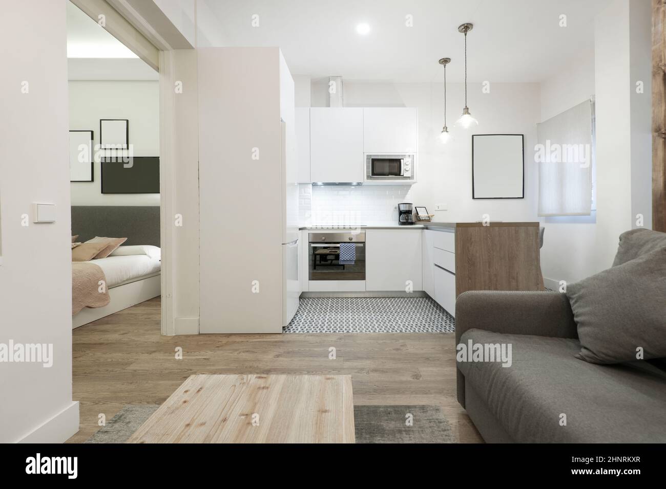 Estudio con sala de estar cocina equipada con sofá cama, muebles blancos y suelo madera Fotografía de stock - Alamy