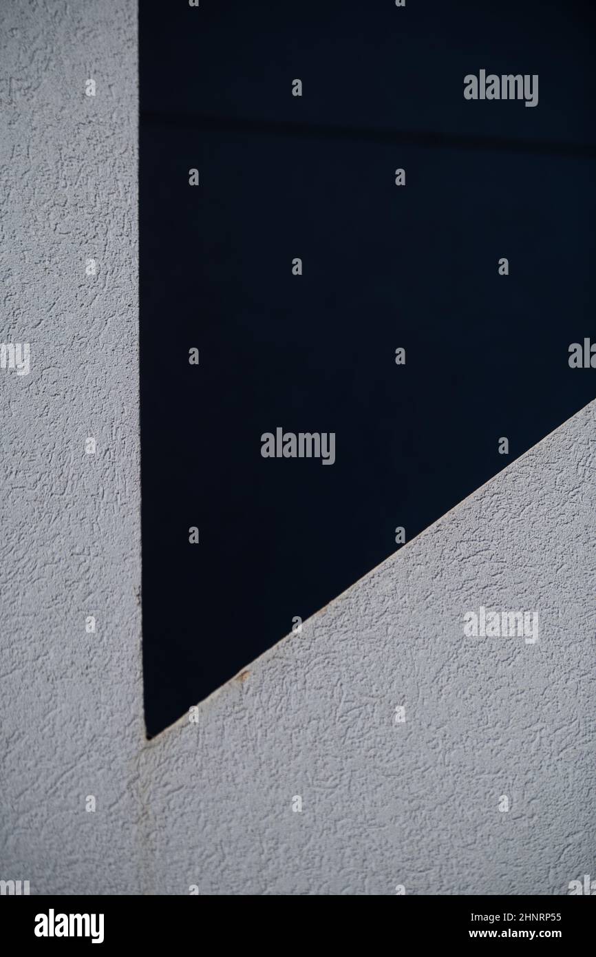 diseño abstracto de sombras en la pared exterior gris blanca del edificio creando formas geométricas en ángulos y líneas en blanco y negro con fondo vertical Foto de stock