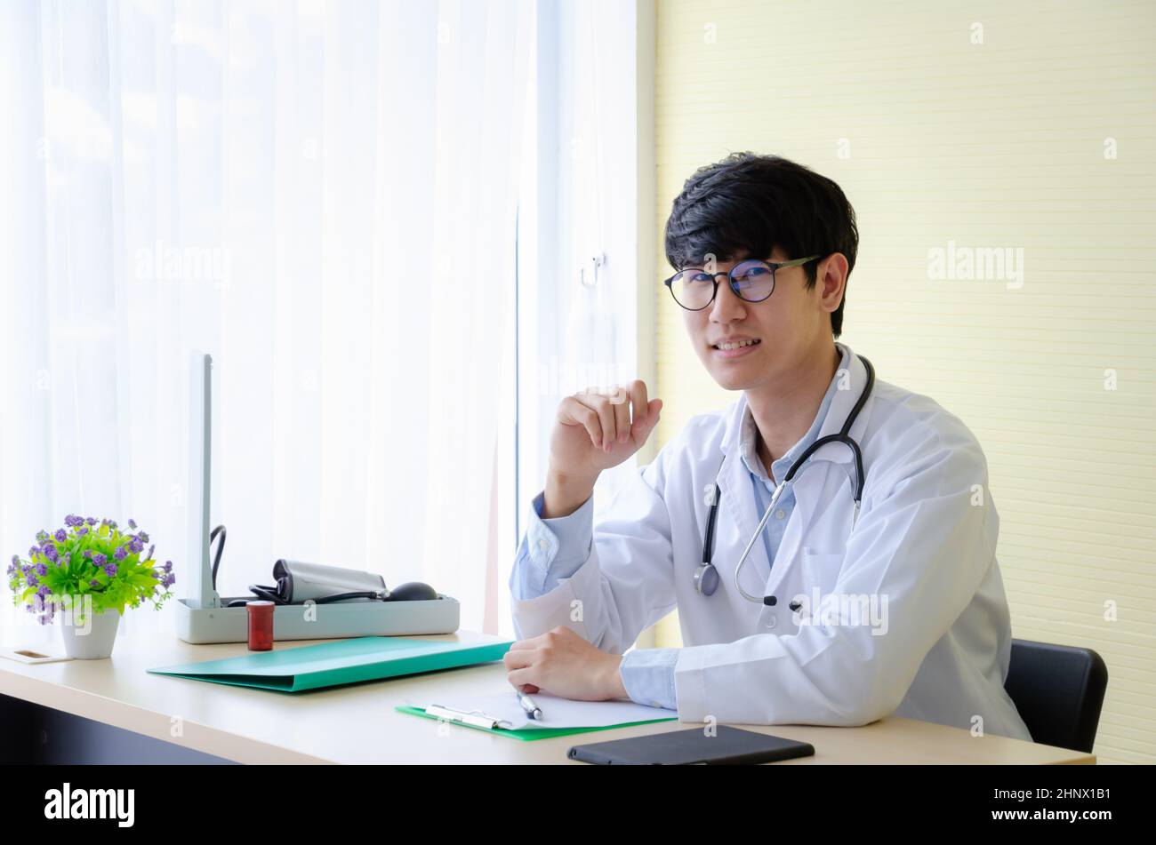 Retrato de un médico masculino en anteojos sentados en el escritorio. Un joven médico sonriente esperando a un paciente en el consultorio del hospital. Concepto de salud. Foto de stock