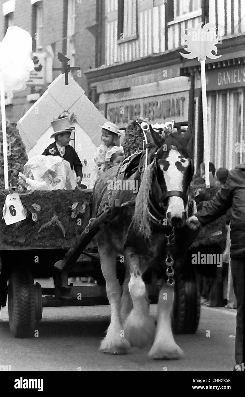 La procesión anual del Día Real de Mayo de Knutsford en 1976 en Knutsford, Cheshire, Inglaterra, Reino Unido. Tradicionalmente incluye un concurso de disfraces de niños con trajes históricos o legendarios con carruajes tirados por caballos. Aquí los niños pequeños, un niño y una niña con vestido de lujo, en un carro de granja, son tirados por un carphorse. Foto de stock