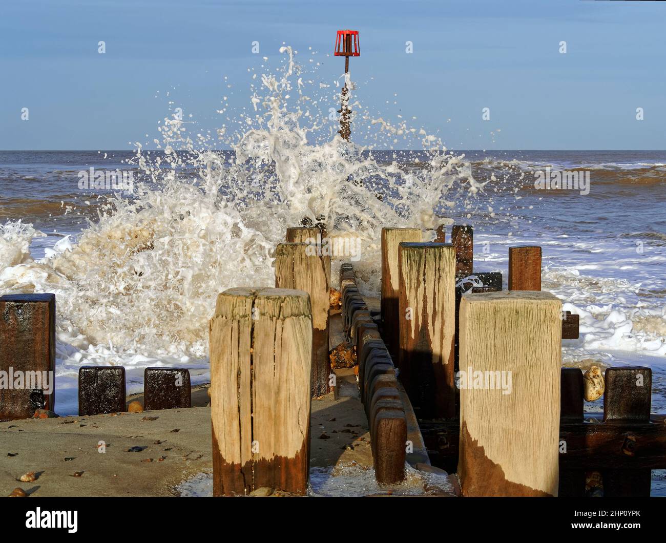 Olas rompiendo sobre defensas marinas de madera en Walcott, Norfolk, durante mares ásperos después de una tormenta que causa rocío y espuma de mar. Foto de stock