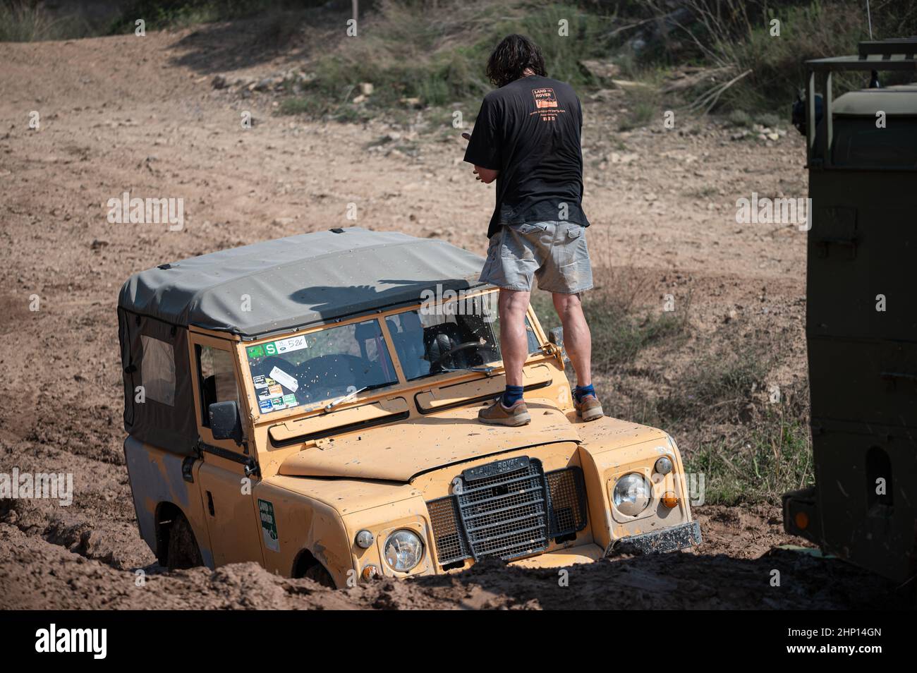 Primer plano de un viejo Land Rover Santana Serie III amarillo con un hombre parado en la parte superior del capó Foto de stock