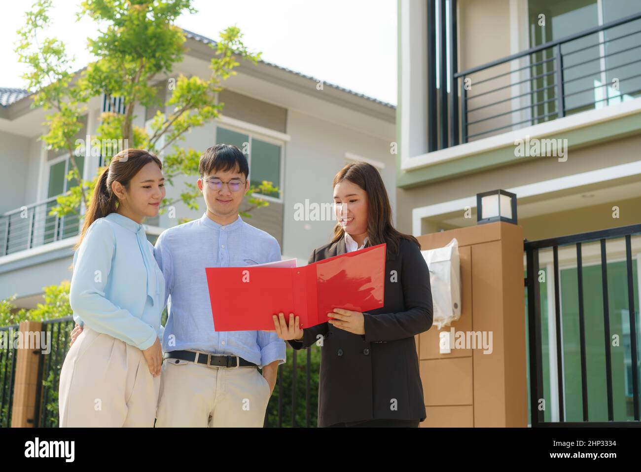 Mujer asiática agente inmobiliario mostrando un detalle de la casa en su archivo a la joven pareja asiática amante mirando e interés para comprarlo. Comprar una nueva h Foto de stock