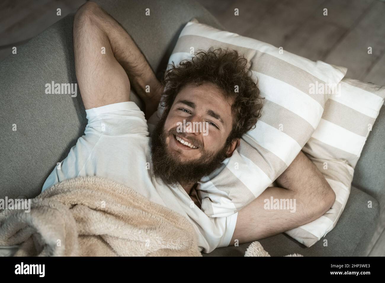 Primer plano. Retrato de un hombre relajado y hermoso cabello rizado durmiendo en el sofá o en el sofá disfrutando de los fines de semana o los días de cuarentena en casa. Fin de semana relájese en casa. Foto de stock