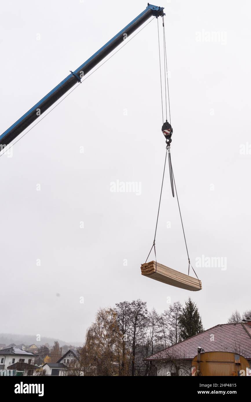 La grúa de carga lleva la madera al lugar de construcción - grúa en la construcción de la casa Foto de stock