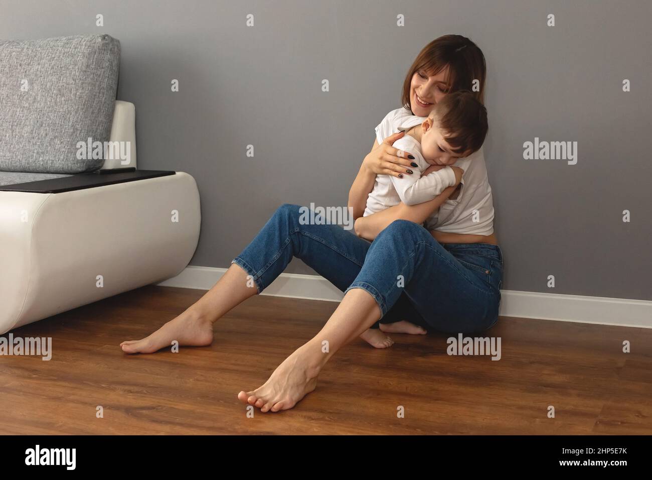 La madre y el bebé se sientan en el suelo de la habitación, abrazándose suavemente unos a otros Foto de stock