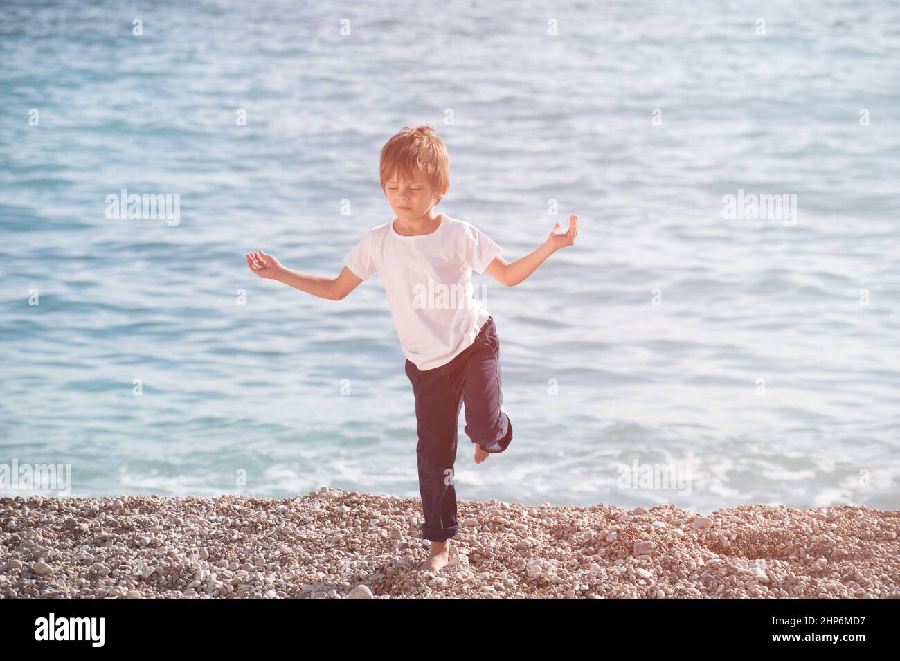 estado mental meditativo durante la práctica de meditación de yoga de ocio del niño pequeño en punto blanco en la orilla del mar al atardecer Foto de stock