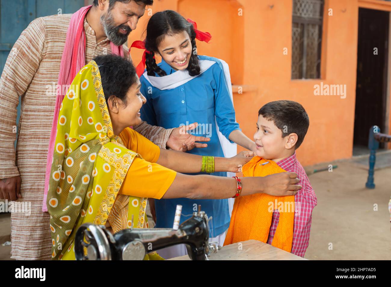 La madre india comprueba el tamaño de las telas en su hijo mientras el  marido y la hija lo miran, coser telas en la máquina de coser. Familia  pequeña, estilo de vida