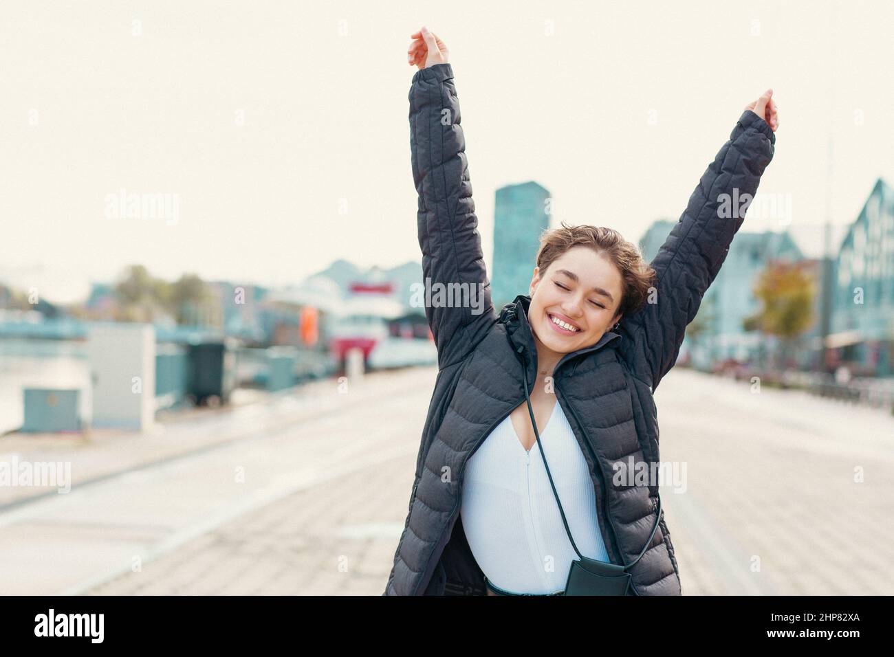 Joven mujer feliz con sus manos levantadas disfrutando del tiempo al aire libre, hora dorada Foto de stock