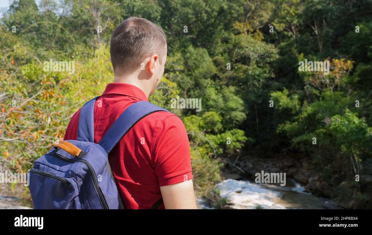 Hombre de viaje en polo rojo con mochila cerca del río rock Foto de stock