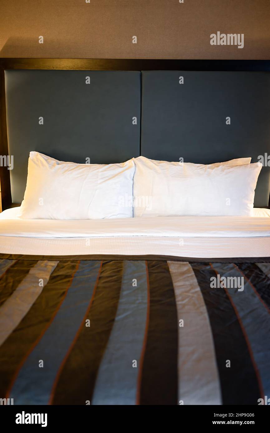 Habitación de dormitorio por la noche con almohadas blancas y sábanas en el colchón vista frontal de la cama en la moderna habitación de hotel motel sin nadie y decoración vertical con estilo Foto de stock