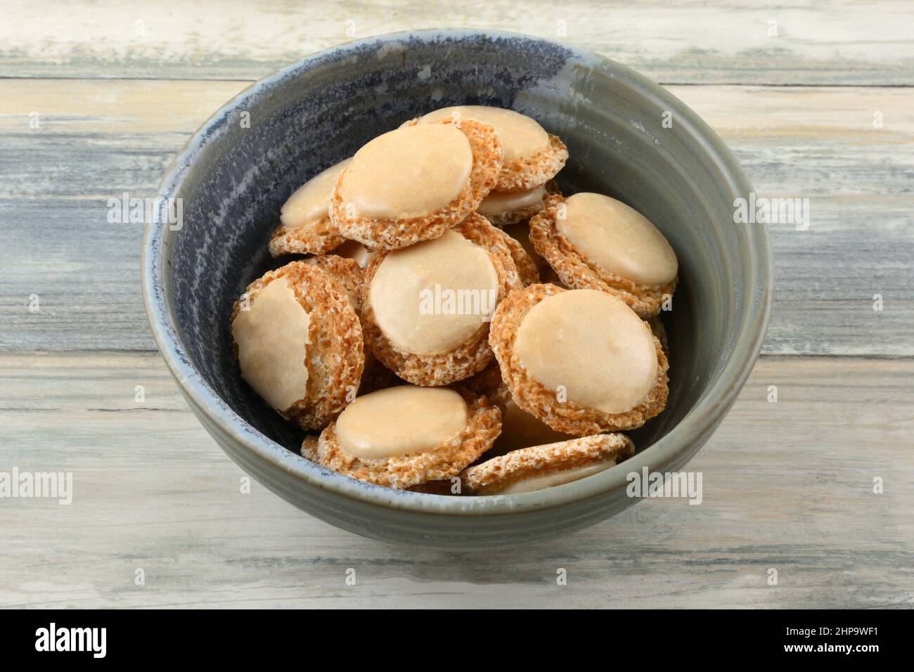 Las galletas de macaron de vainilla y albaricoque también se llaman botones del vientre sagrado en un tazón de cerámica Foto de stock
