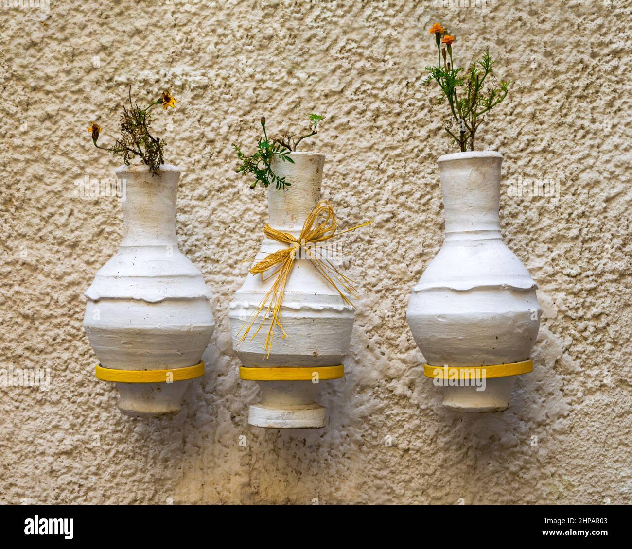 Tres jarrones de cerámica blanca hechos a mano adyacentes, árabe: Kolla, colgado en pared blanca de piedra áspera Foto de stock
