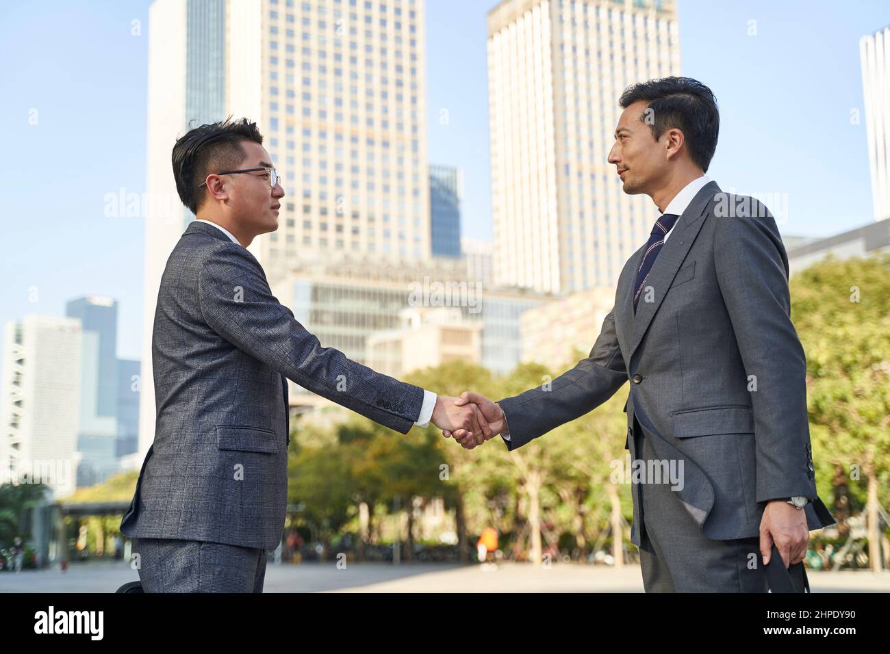 hombres de negocios asiáticos que se reúnen al aire libre sacudiendo las manos Foto de stock