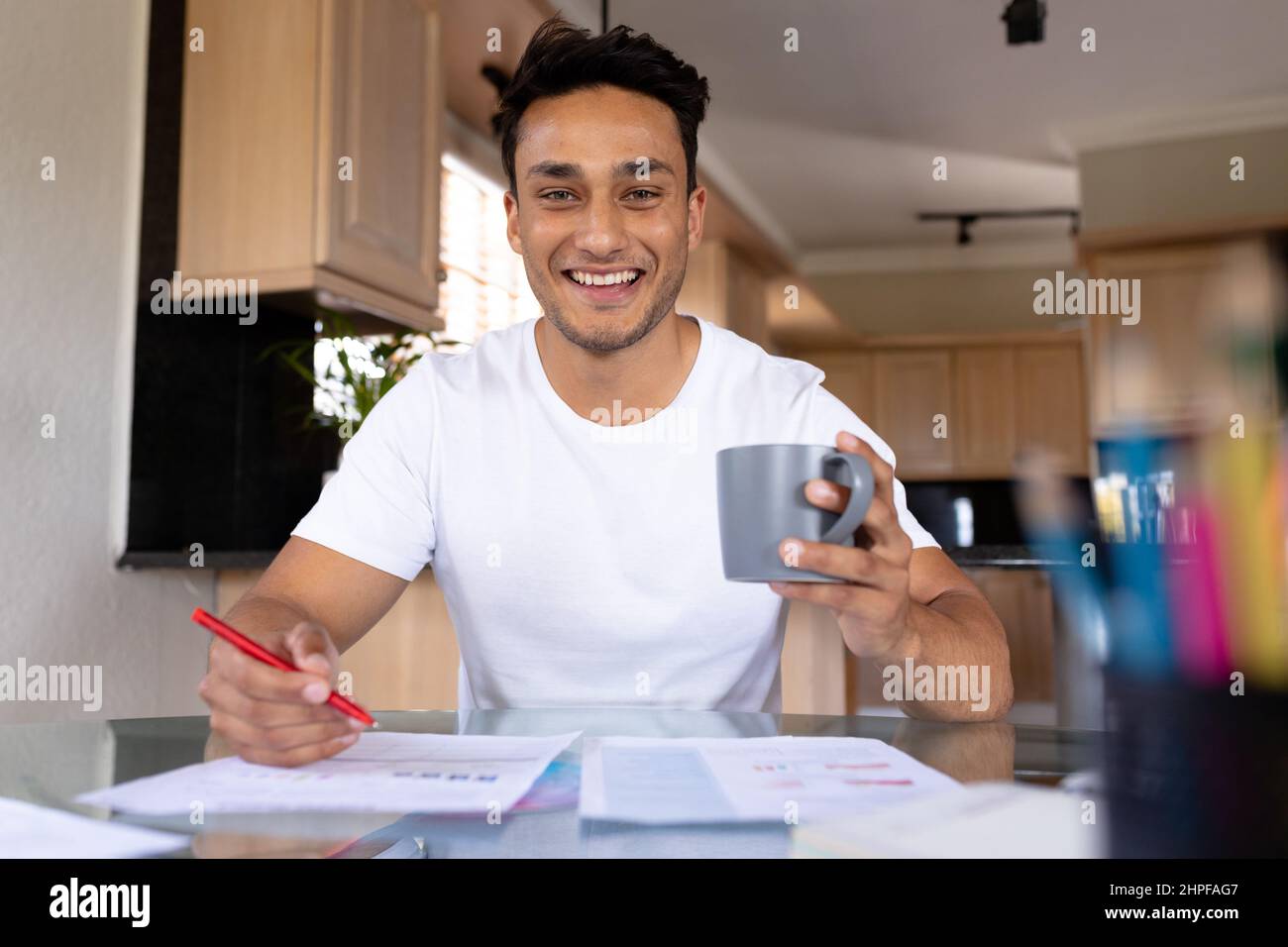 Retrato de feliz hombre biracial freelancer sosteniendo taza telecommuting en la oficina de casa Foto de stock