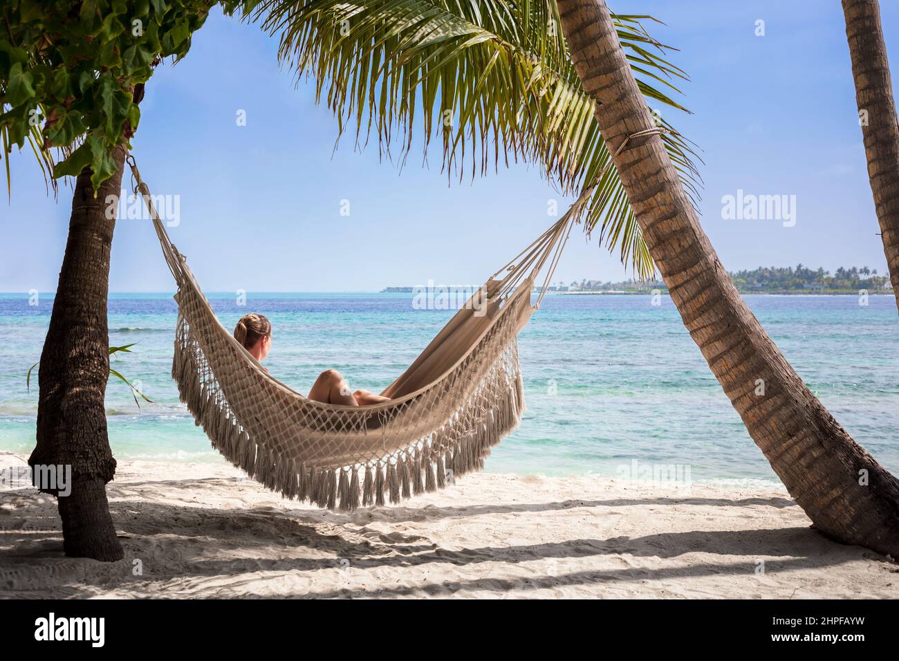 Vacaciones en la playa con una mujer relajándose en una hamaca entre palmeras de coco, arena blanca, cielo azul y agua turquesa. Escénico complejo turístico en la isla de Ma Foto de stock