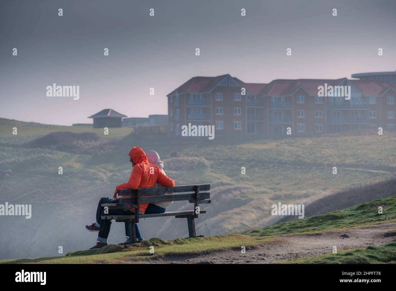 Una pareja sentada en un banco con sus capuchas a viento fuerte traída por Storm Eunice en Newquay en Cornwall Reino Unido. Foto de stock