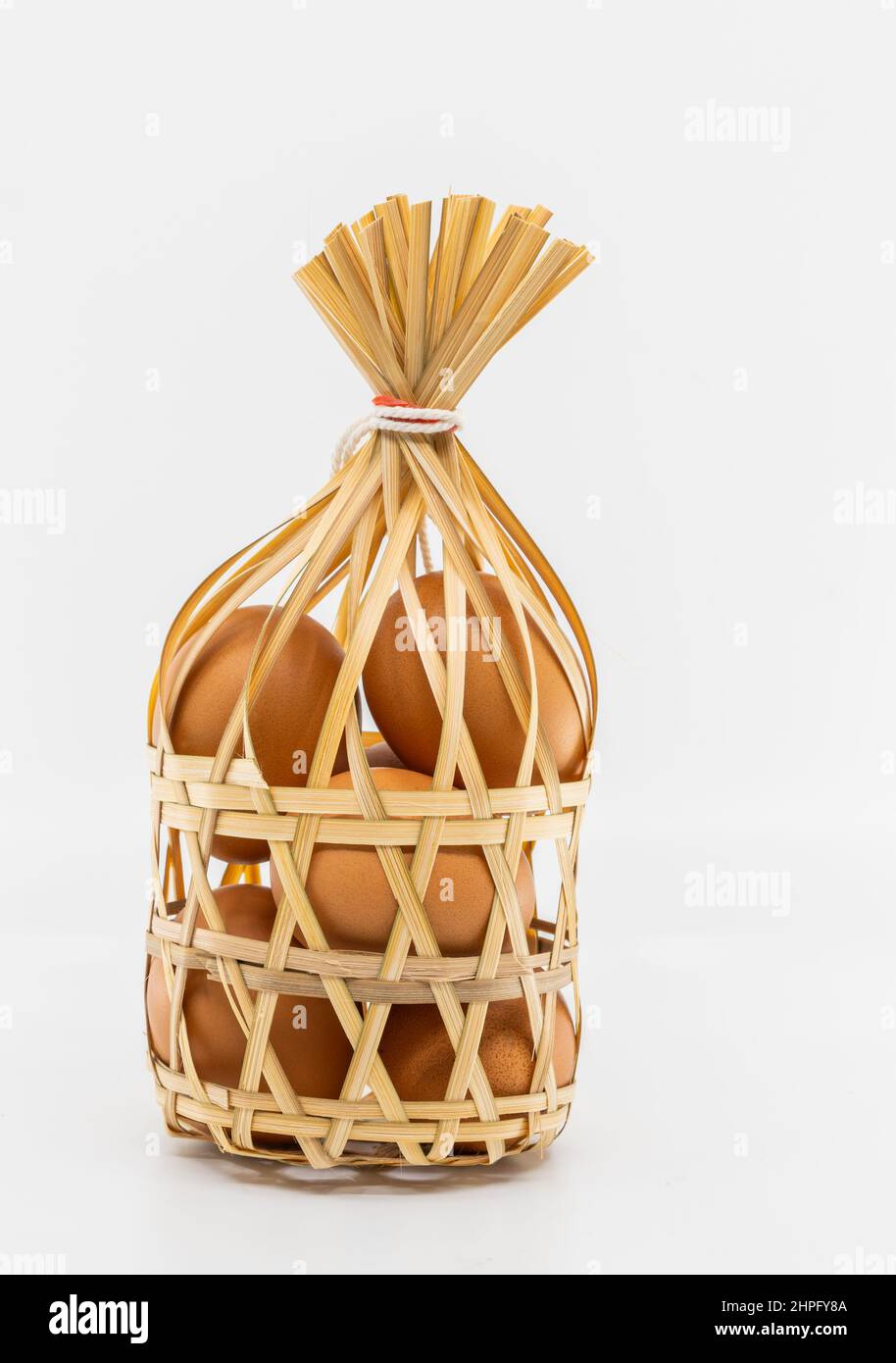 Huevos de pollo marrón orgánico aislados en una cesta redonda de mimbre de bambú sobre fondo blanco, vista frontal de la imagen. El concepto para una alimentación saludable. Foto de stock
