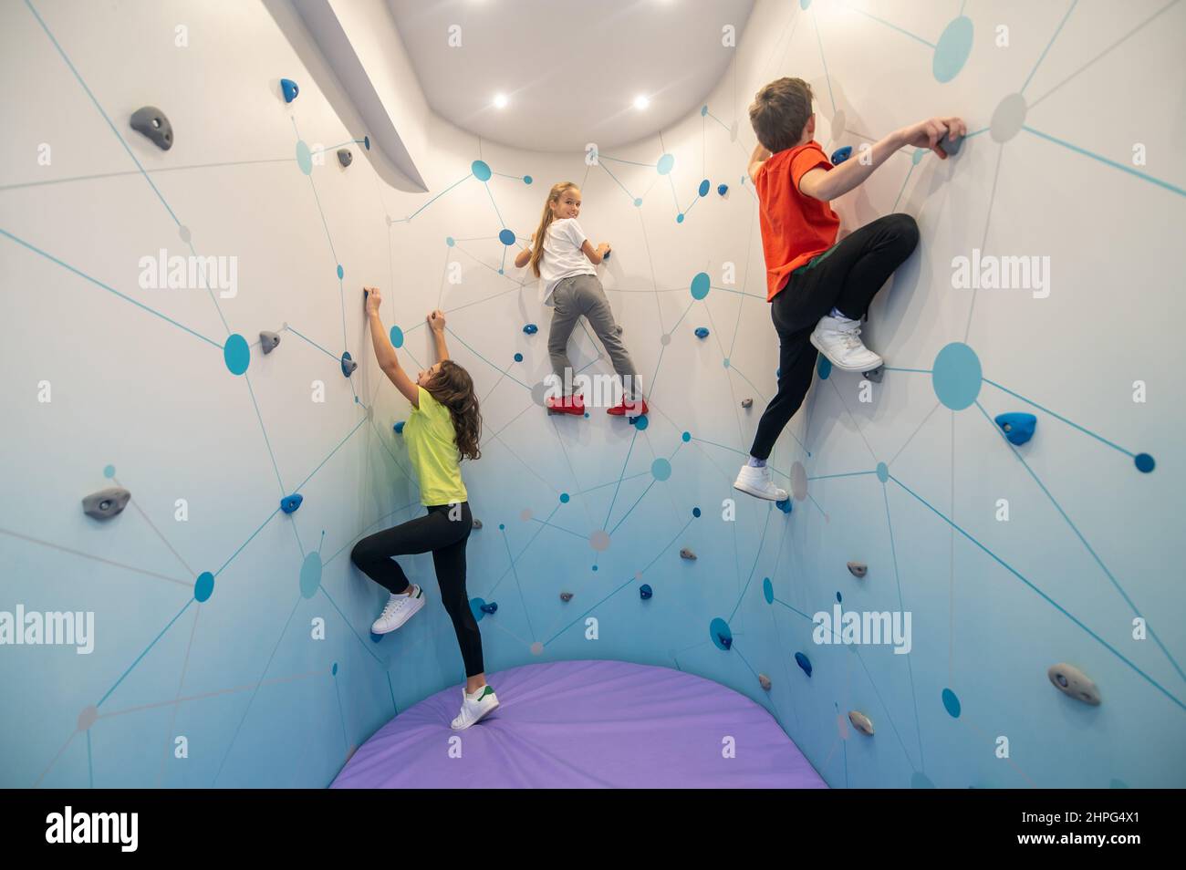 Dos niñas y un niño subiendo la pared en el entrenamiento Foto de stock