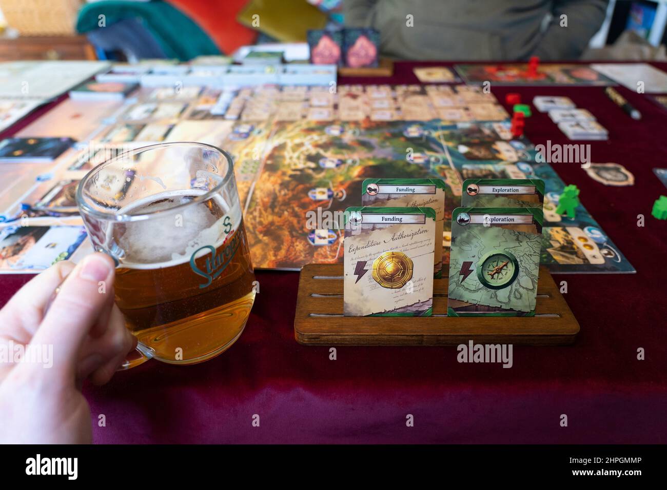 Un hombre de 40 años bebiendo una cerveza y mirando sus cartas para jugar a las Ruinas Perdidas de Arnak juego de mesa. Tema: Juegos y pasatiempos para adultos. REINO UNIDO Foto de stock