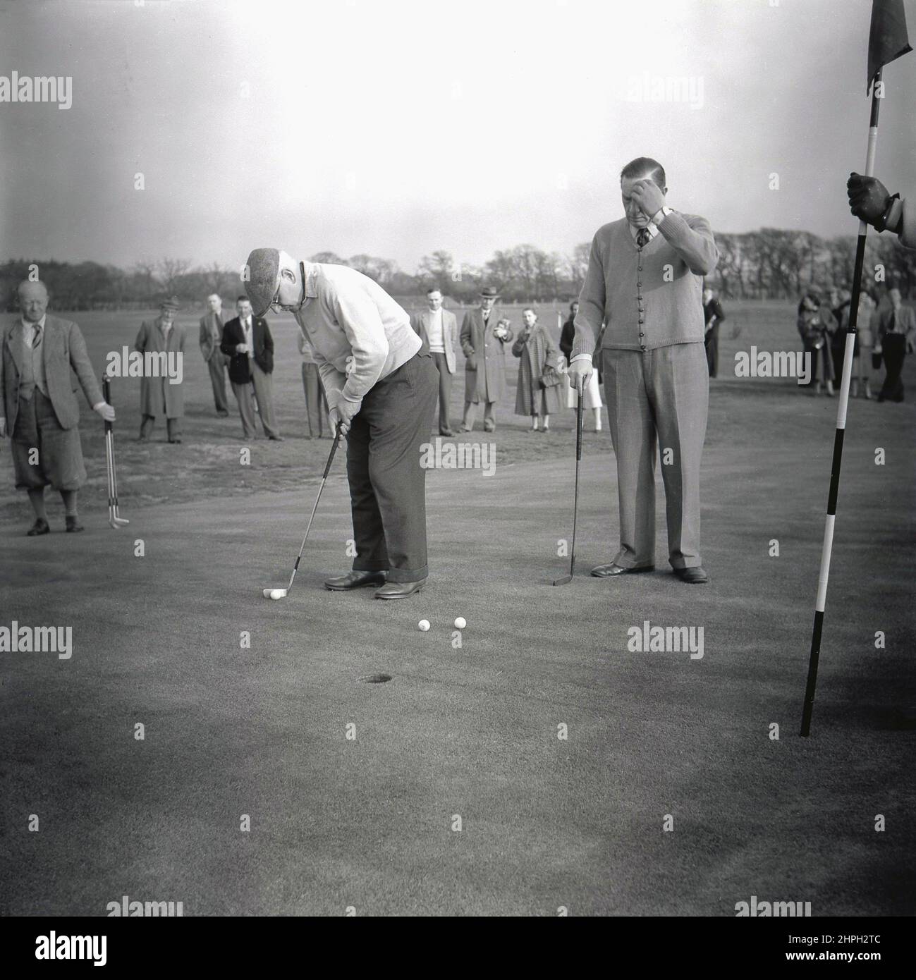 1950s, histórico, jugando en un día de golf de la compañía, dos golfistas masculinos en un verde del puttin, uno a punto de poner su bola hacia el agujero, Puerto Talbot, Gales, Reino Unido. Foto de stock