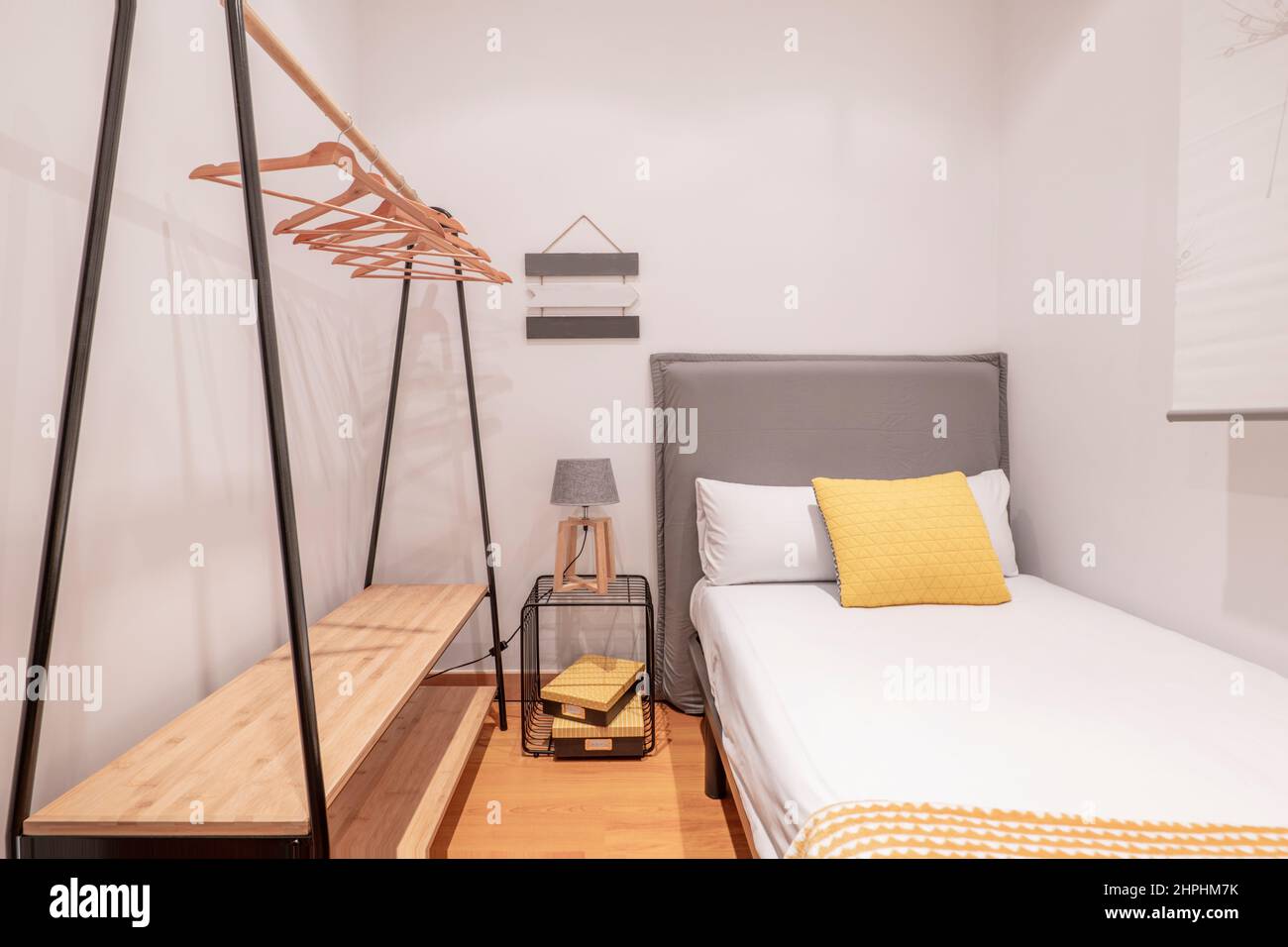 Dormitorio juvenil con cabecero tapizado, cojín amarillo, suelos de madera  y caballete con perchas de madera Fotografía de stock - Alamy