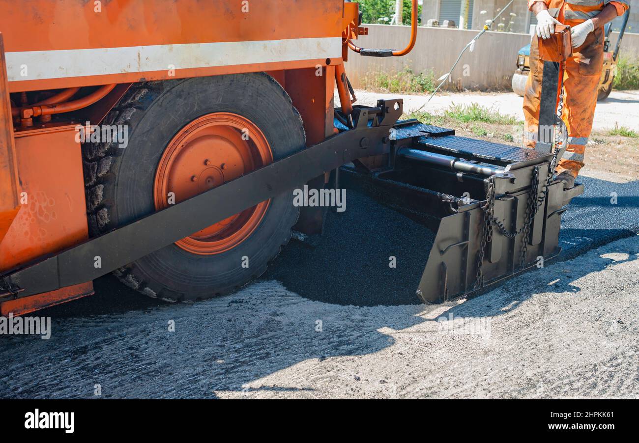 Seguimiento regular del trabajador pavimentadora asfaltado calentado a temperaturas superiores a 160 ° en una pista de pavimento Foto de stock