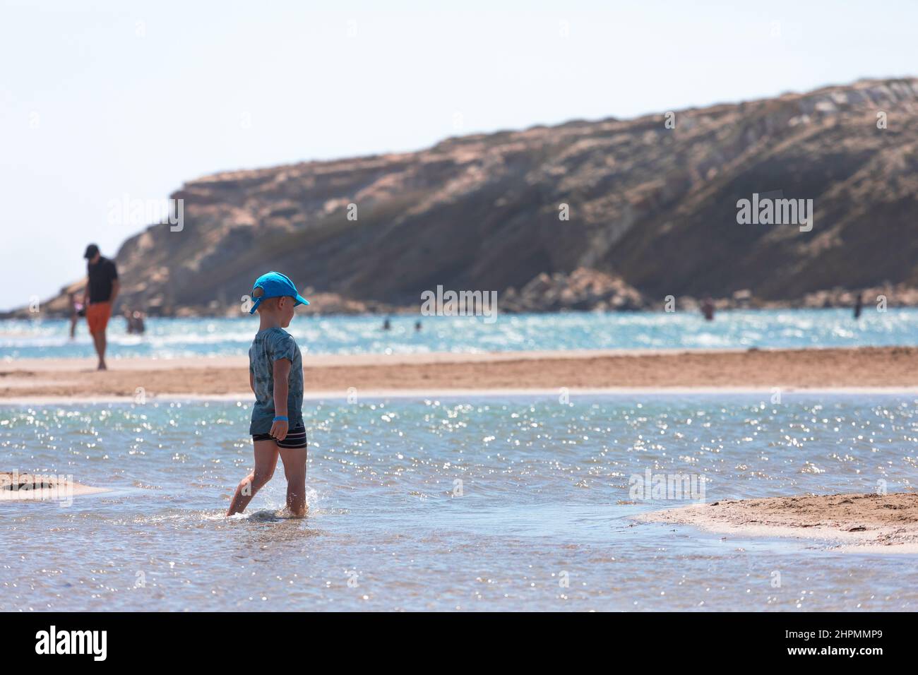 Un niño está parado en la playa del Cabo Prasonisi en Grecia y observa un kitesurf volando en el horizonte Foto de stock