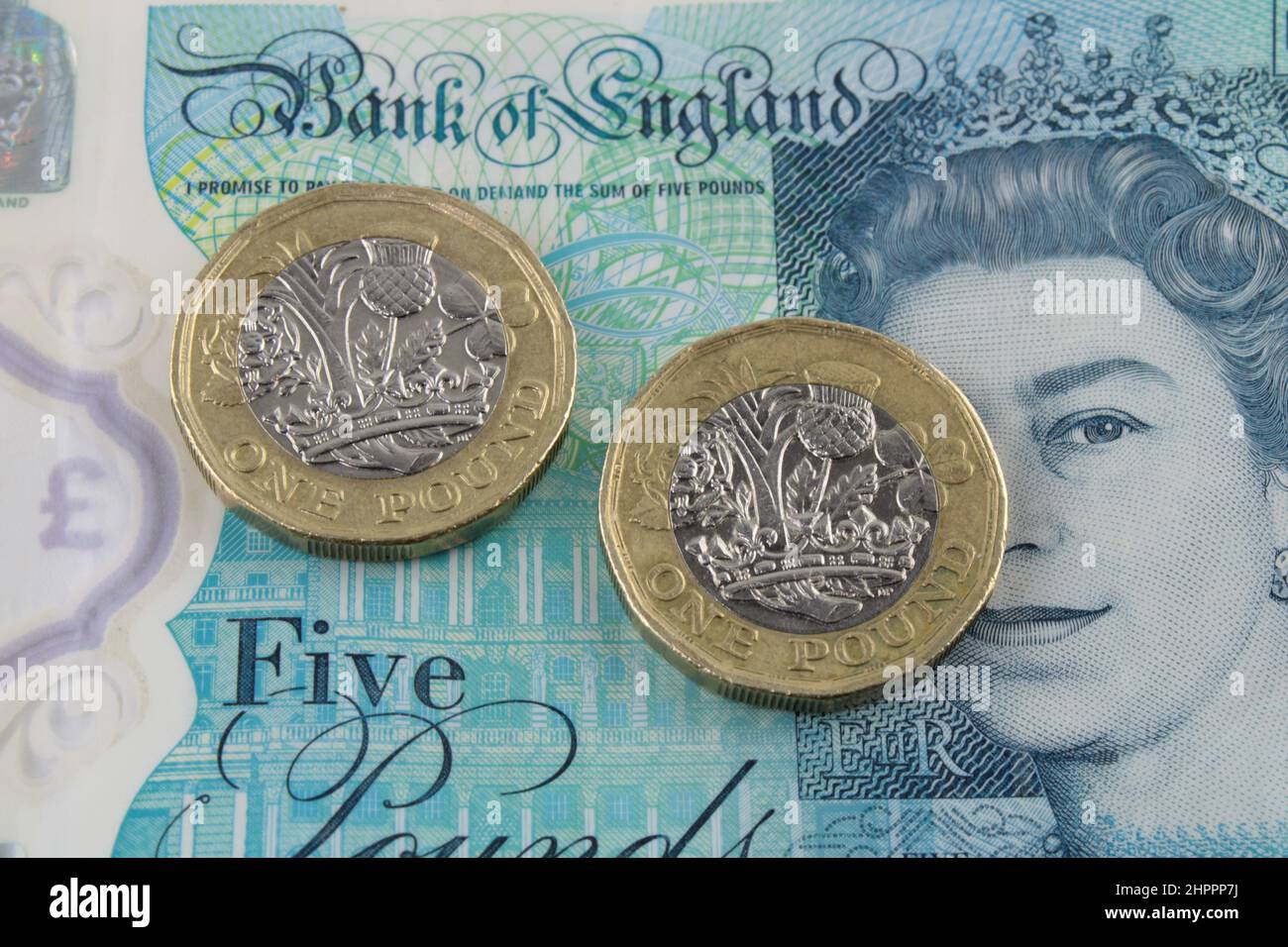 Monedas de libra británica sobre un fondo de nota de cinco libras. Concepto de economía, deuda y recesión. Foto de stock