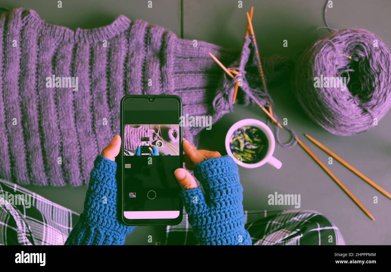 Vista superior mujer mano ropa de ganchillo azul mitten, punto jersey violeta para regalo en invierno, cierre mano prensa smartphone para hacer fotos en tonos oscuros Foto de stock