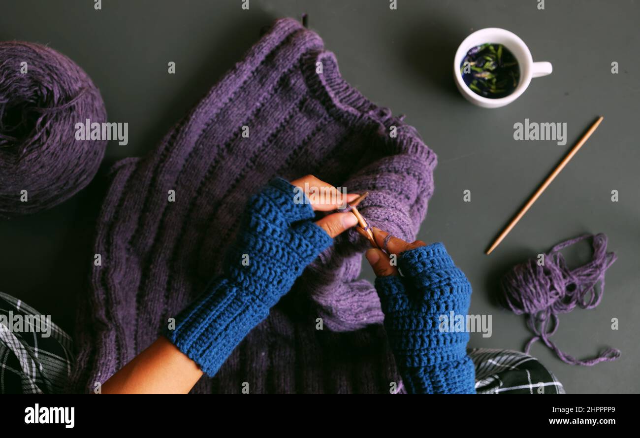 Vista superior mujer mano ropa de ganchillo azul mitten, punto jersey violeta para regalo en invierno, cierre mano prensa smartphone para hacer fotos en tonos oscuros Foto de stock