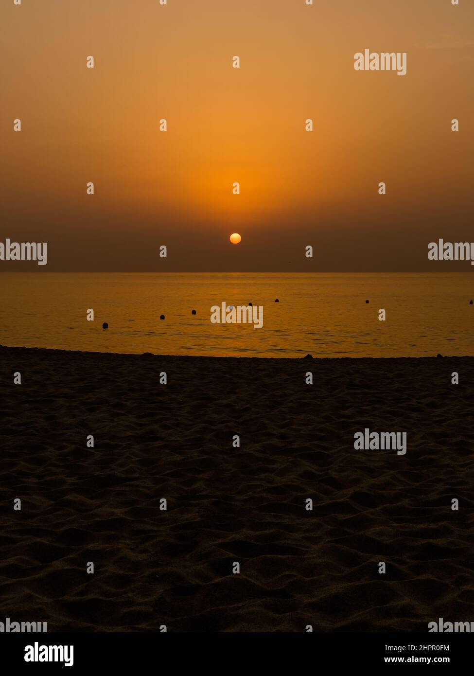 El sol anaranjado se levanta lentamente en el horizonte durante el amanecer con la arena en la playa en el primer plano todavía oscura. Foto de stock