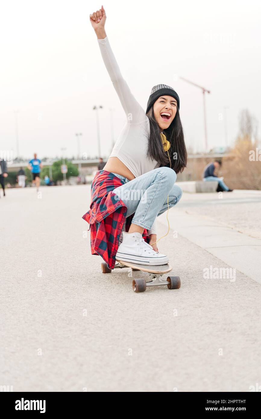 la joven latina disfrutándose mientras montaba en una tabla de skateboard. la chica hispana pasa su tiempo libre haciendo deportes al aire libre. Foto de stock