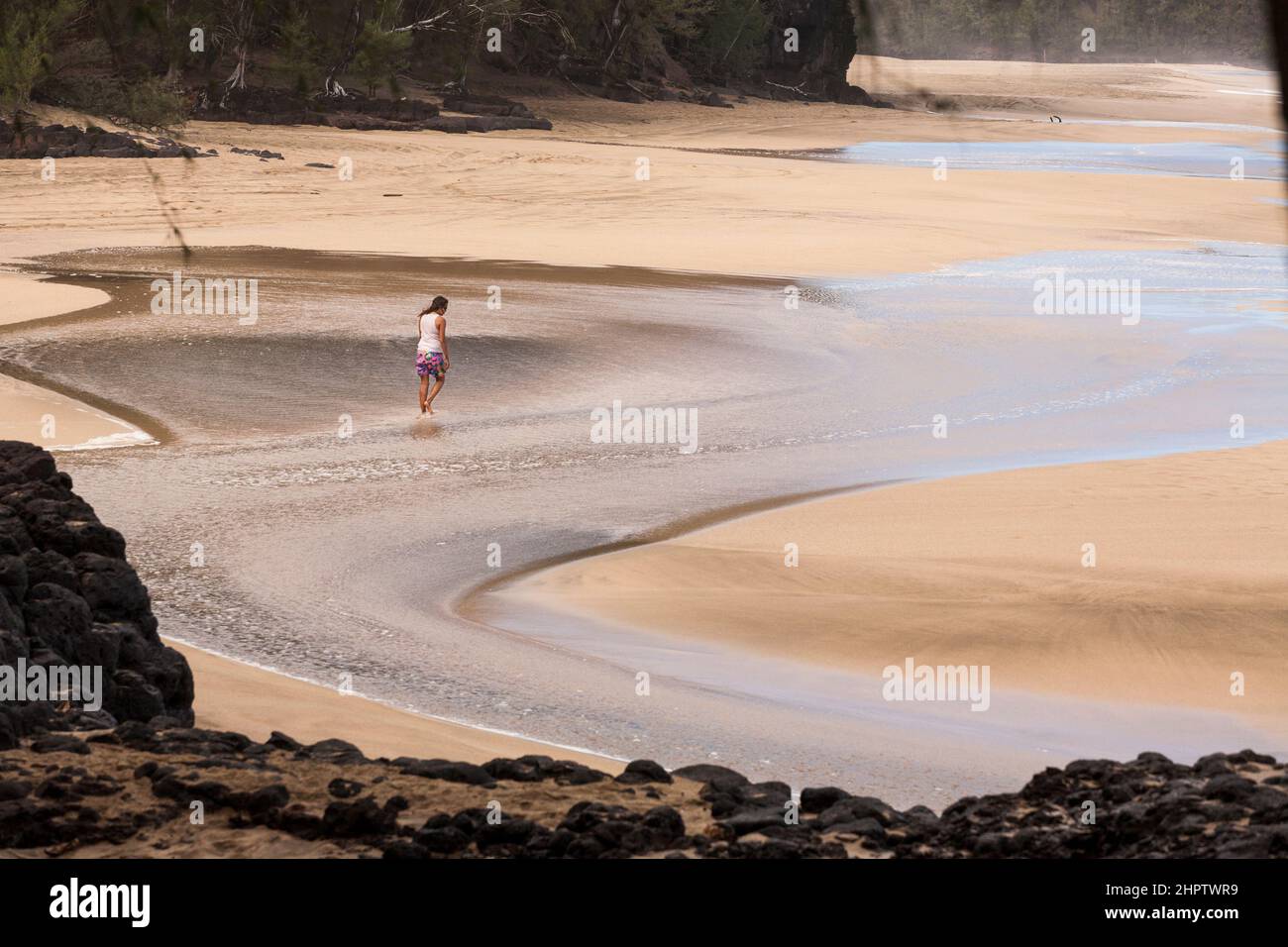 Caminando por la playa Buscando: Una mujer camina sola a través de un arroyo de olas en esta famosa playa aparentemente buscando el agua a sus pies. Foto de stock