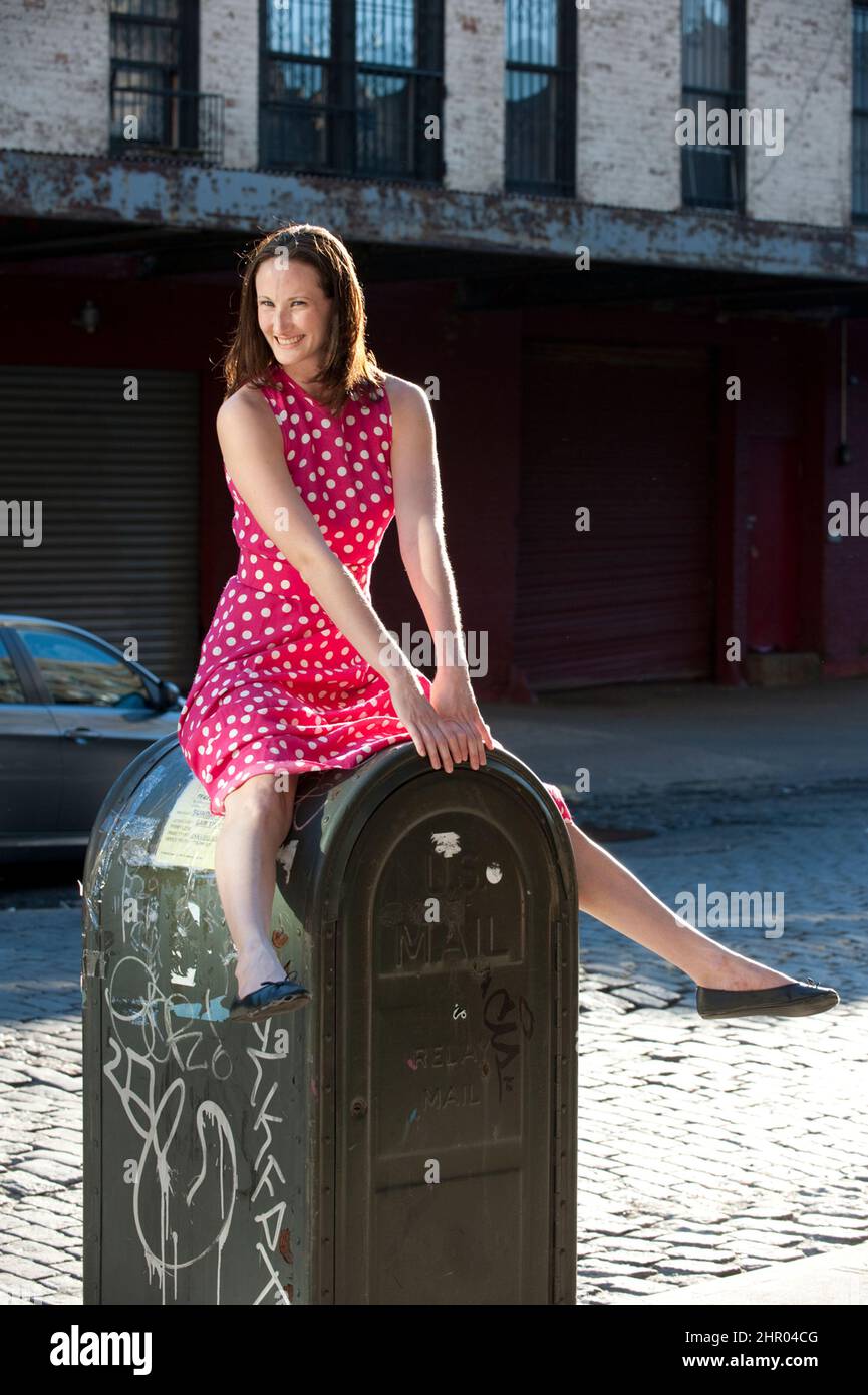 Mujer joven caucásica con un vestido de polkadot rosa posando sobre una caja de correo Foto de stock