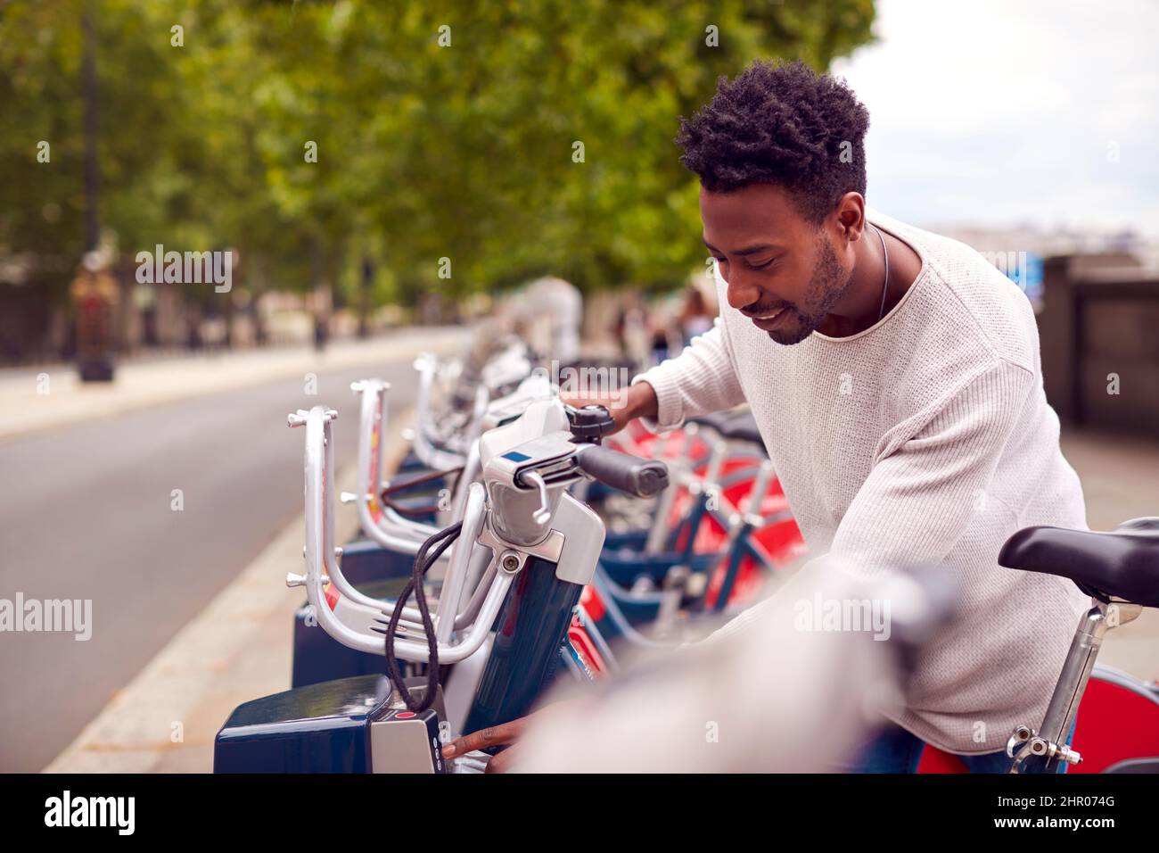 Hombre joven Alquiler de bicicletas como forma verde de transporte para moverse por la ciudad Foto de stock