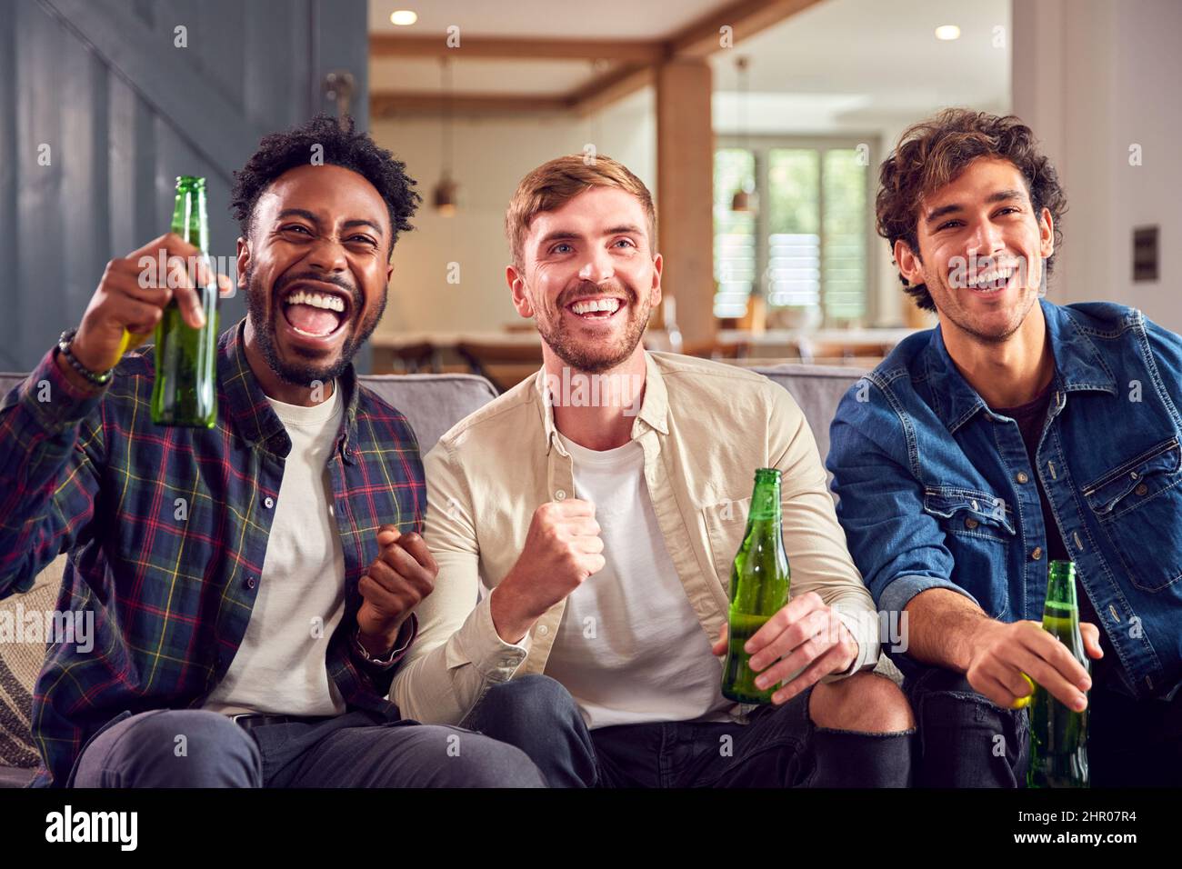 Grupo multicultural de amigos masculinos viendo juegos deportivos en la televisión en casa Celebrando un gol con la cerveza Foto de stock