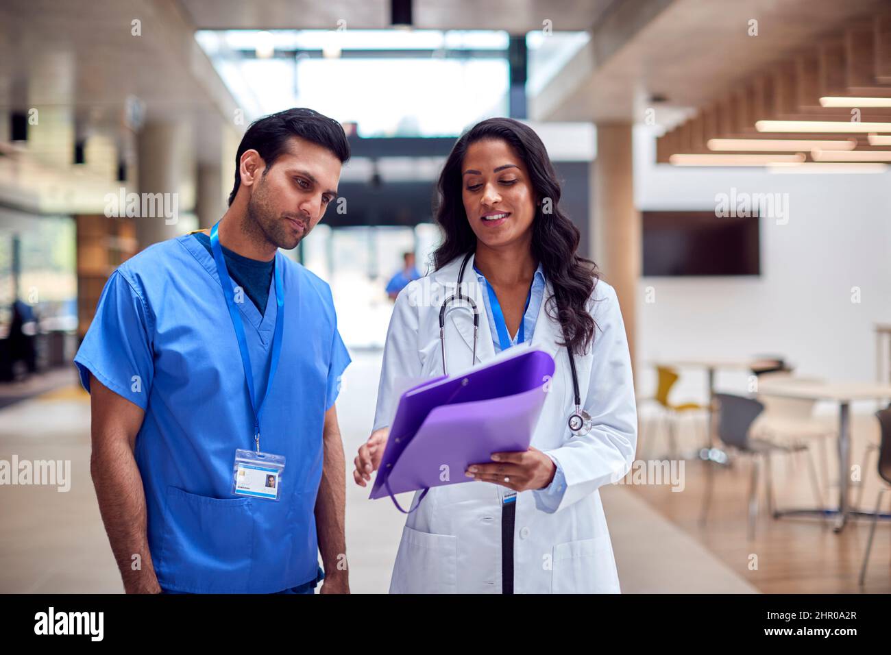 El personal médico de White Coat y Scrubs discutiendo las notas del paciente tienen una reunión informal en el hospital Foto de stock