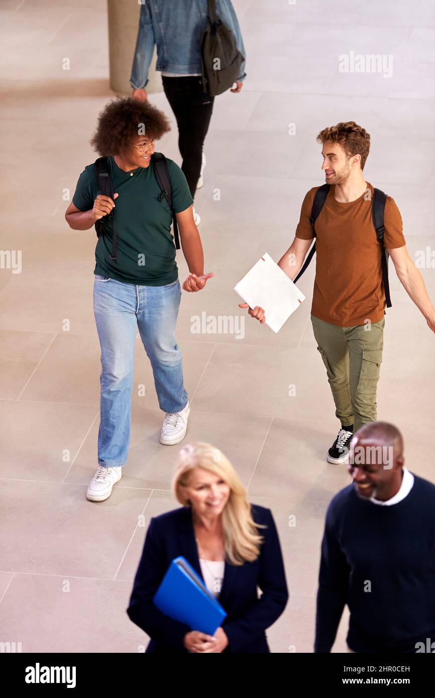 Dos estudiantes masculinos en la universidad ocupada o en el edificio de la universidad que habla mientras caminan a lo largo del corredor Foto de stock