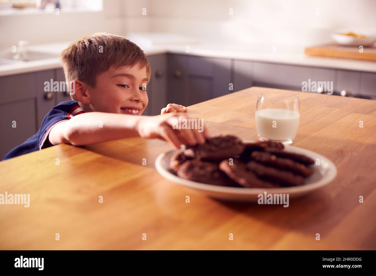 Niño en casa en la cocina que se acerca para tomar galletas del plato en el mostrador Foto de stock